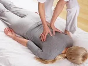 Sur un futon, une jeune femme recoit une séance de shiatsu